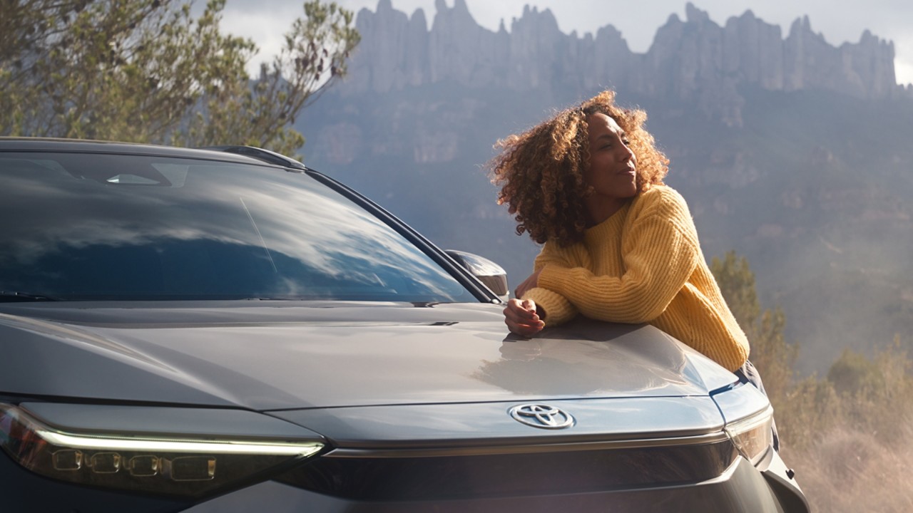 Zrelaksowana młoda kobieta opierająca się o samochód marki Toyota